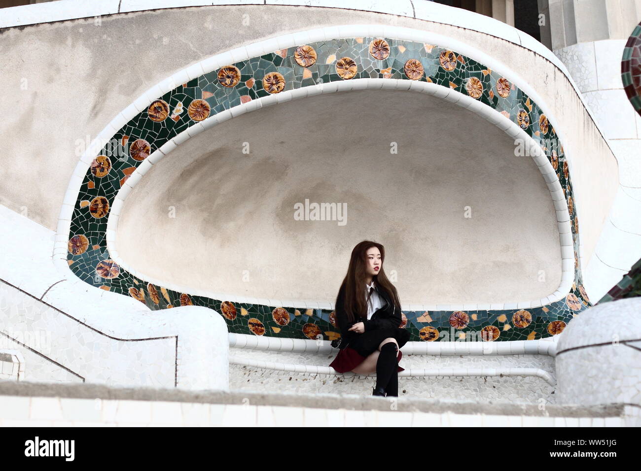 Eine junge asiatische Frau alleine auf einer Bank im Park Güell in Barcelona sitzen, Stockfoto