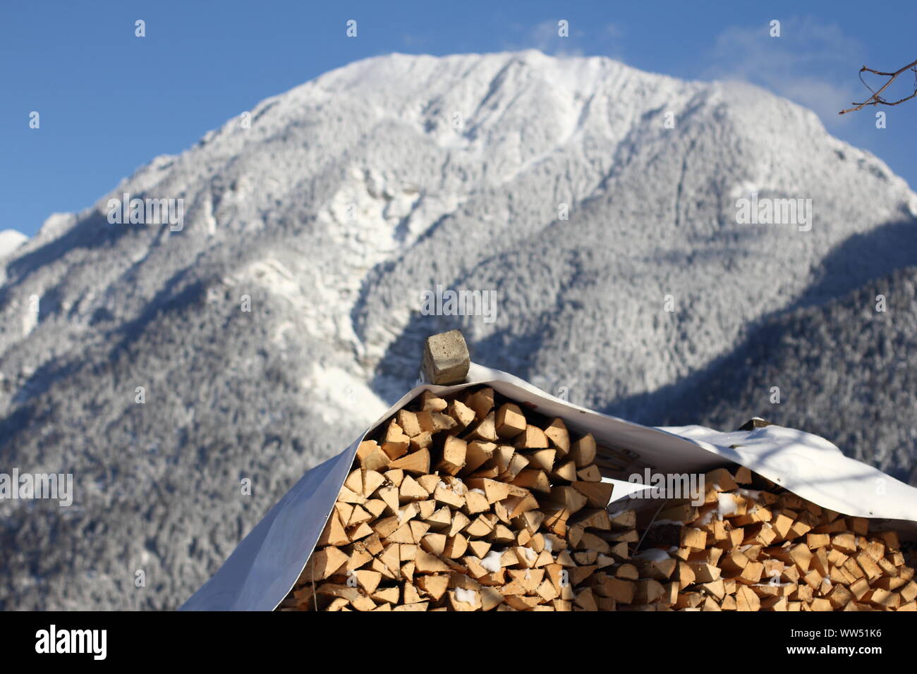 Gestapeltes Holz vor einem schneebedeckten Berge und blauer Himmel in Oberbayern, Stockfoto