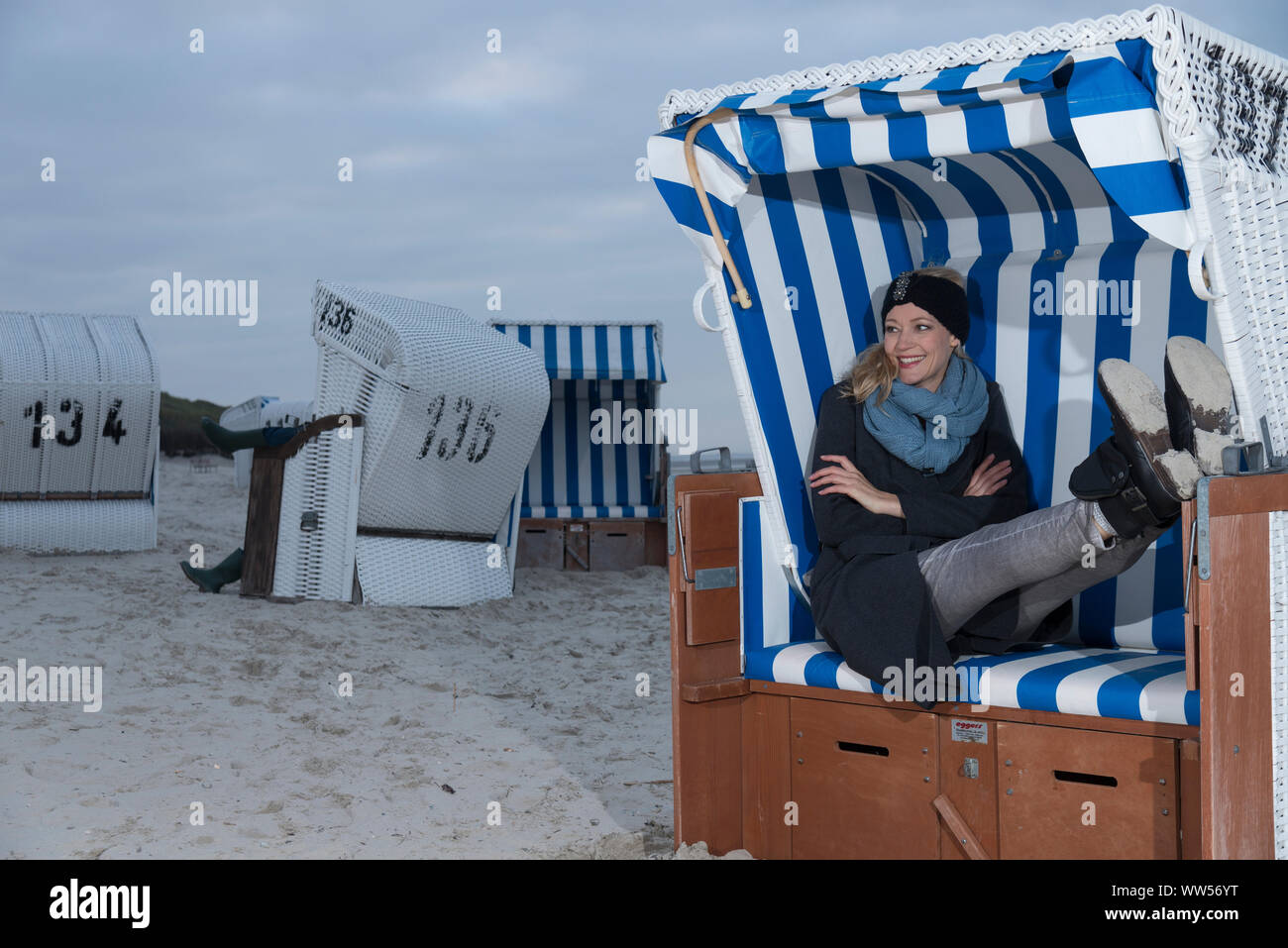 Blonde Frau mit Mantel, Schal und Mantel im Strandkorb sitzen Stockfoto