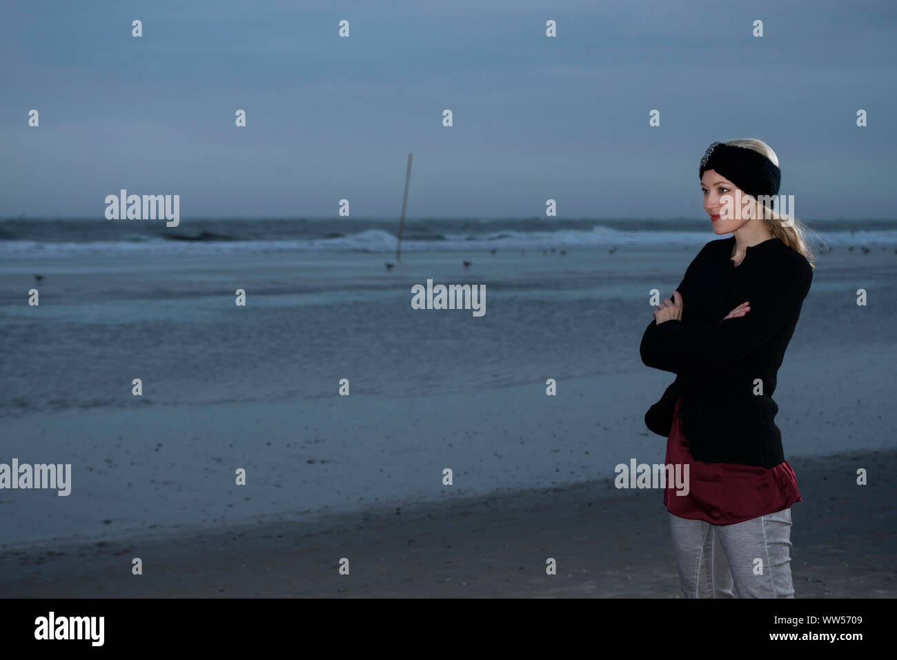 Frau mit Stirnband und Strickjacke in der Dämmerung am Strand Stockfoto