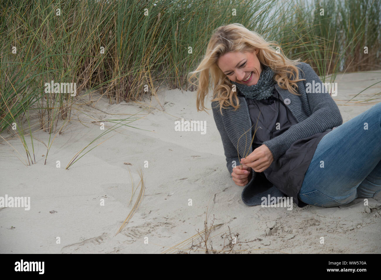 Frau mit blonden Haaren lachend Sitzen im Sand Stockfoto