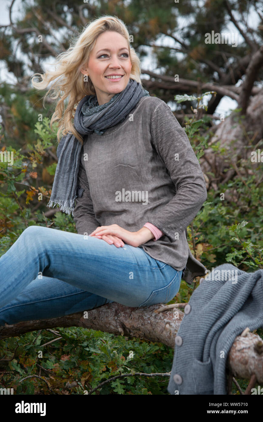 Frau sitzt lächelnd auf umgefallene Baum Stockfoto