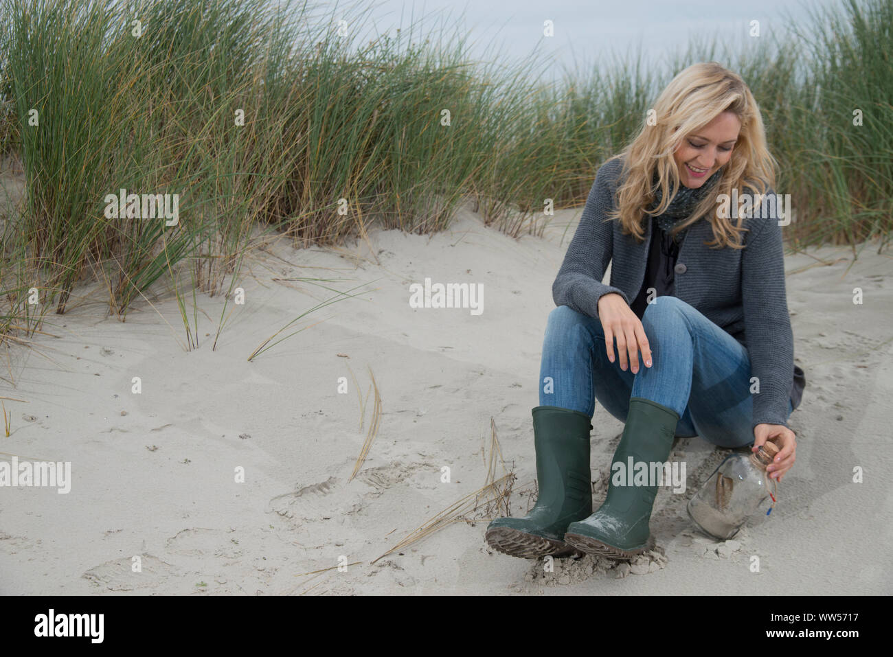 Blonde Frau mit Gummistiefeln und Flasche halb voll Sand Stockfoto