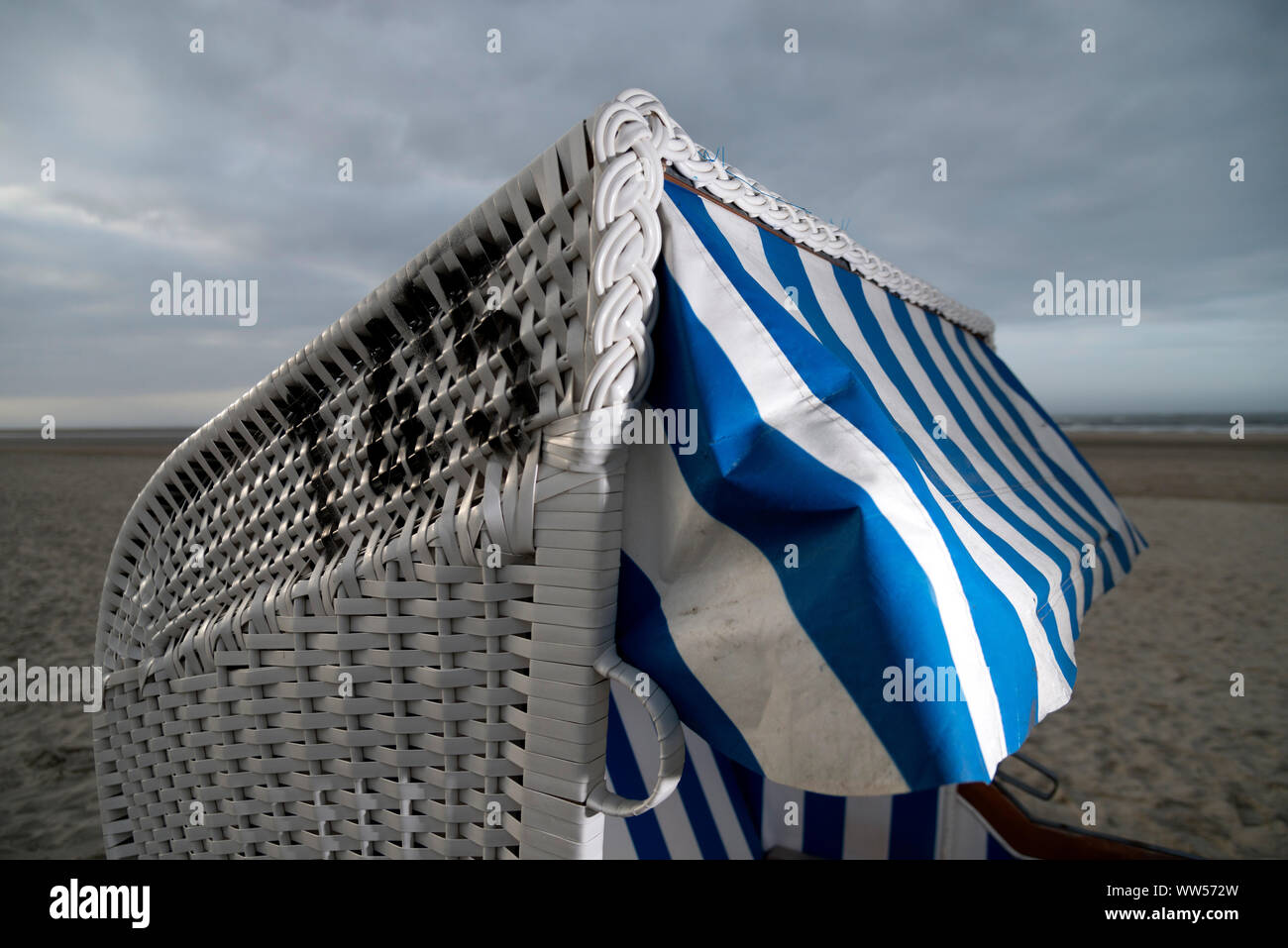 Strandkorb mit blau-weißen Sonnenschutz bewölkt Strand Stockfoto