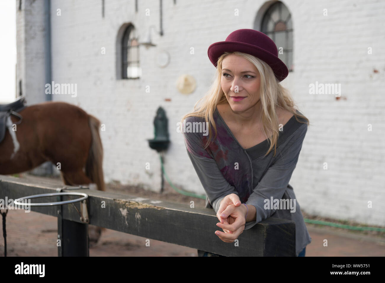 Frau mit Hut lehnte sich auf Zaun, Pferd im Hintergrund Stockfoto