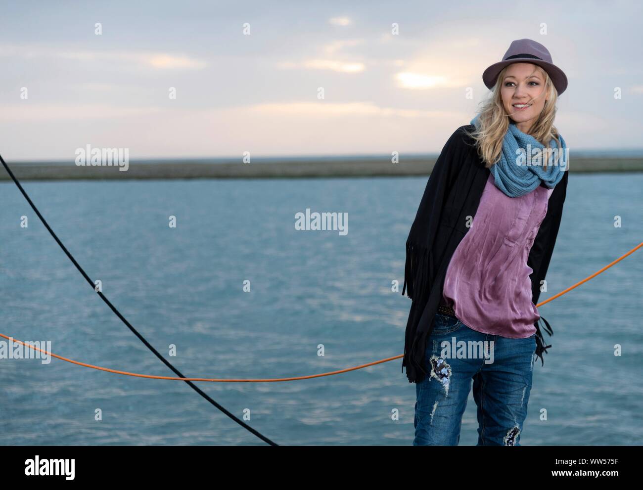 Blonde Frau mit Hut und blauen Schal ständigen Lächeln auf dem Wasser Stockfoto