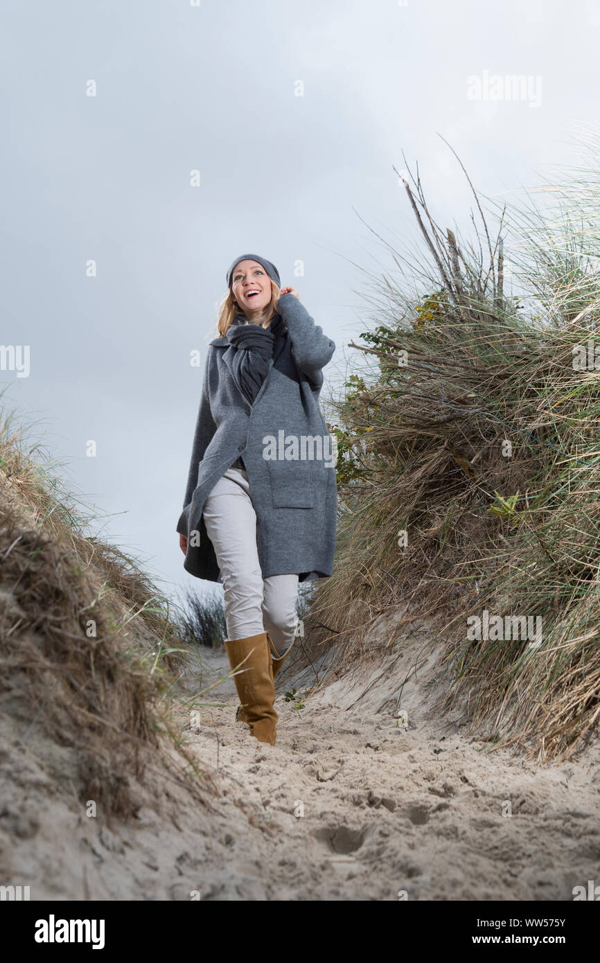 Lachende Frau mit Jacke und Kappe gehen für einen Spaziergang in den Dünen Stockfoto