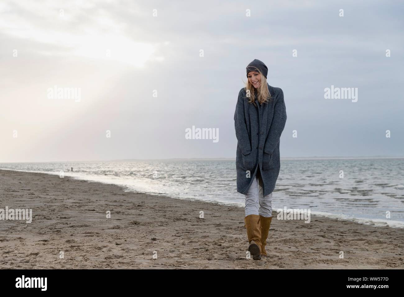 Frau mit Jacke und Kappe zu Fuß am Strand Stockfoto