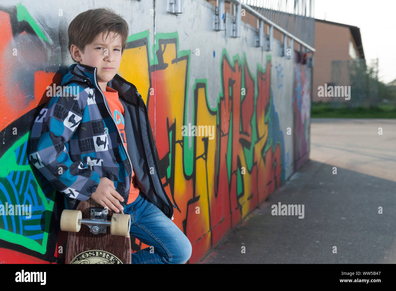 Junge mit Jacke und Skateboard lehnte sich gegen die Wand mit Graffiti Stockfoto