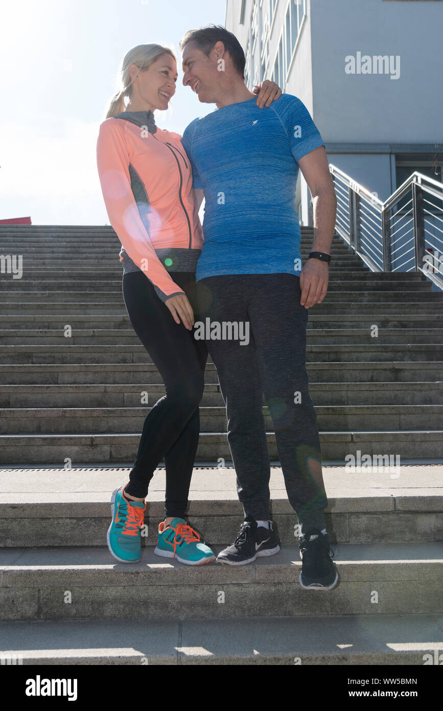 Paar in Sportkleidung auf Treppe außerhalb, Arm in Arm, Lächeln, Blickkontakt Stockfoto