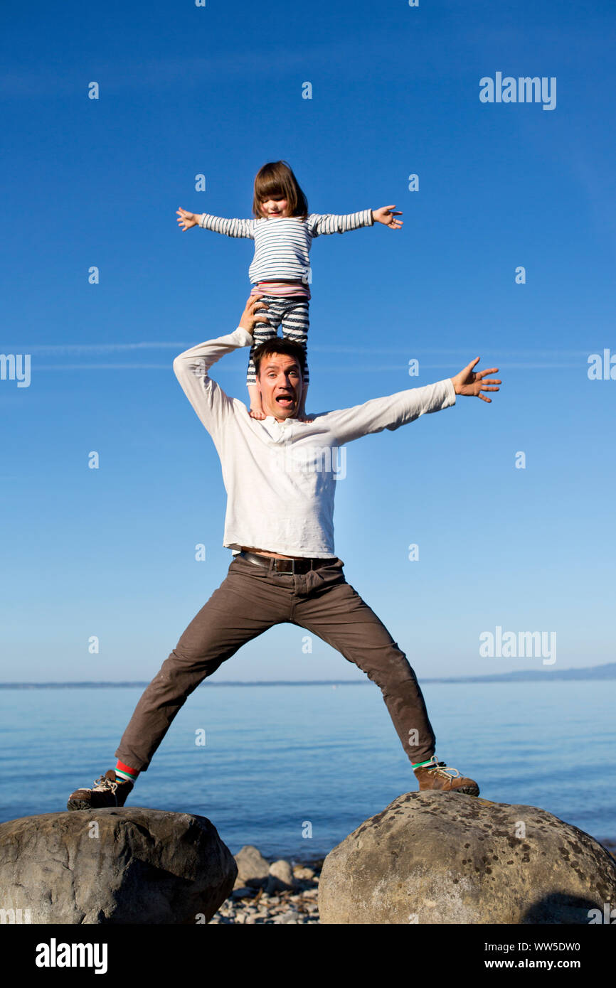 Tochter stehen auf den Schultern ihres Vaters an einem See Stockfoto