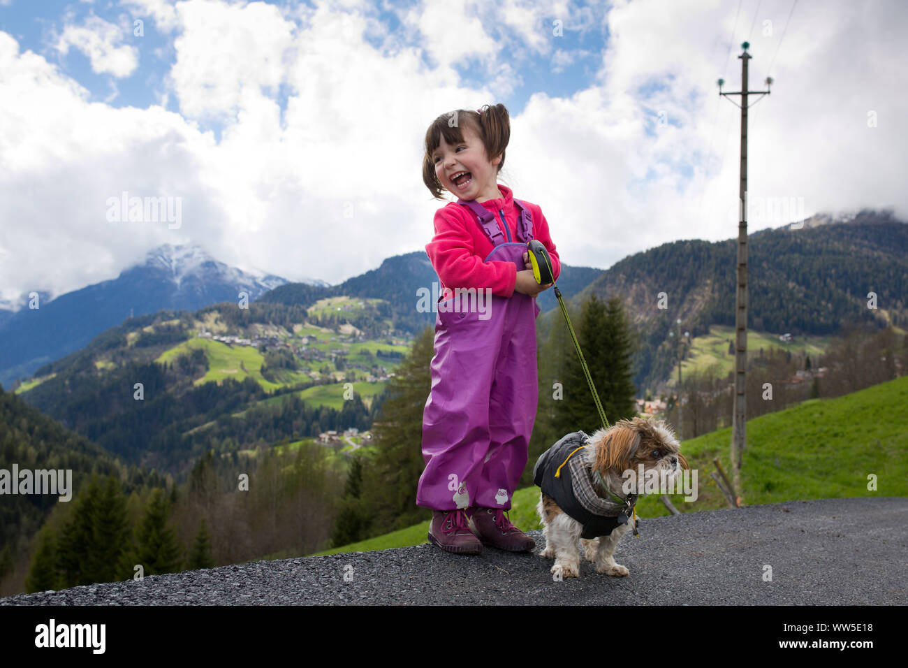 4-6 Jahre altes Mädchen mit Regen Hose und Hund stehen am Straßenrand lacht Stockfoto