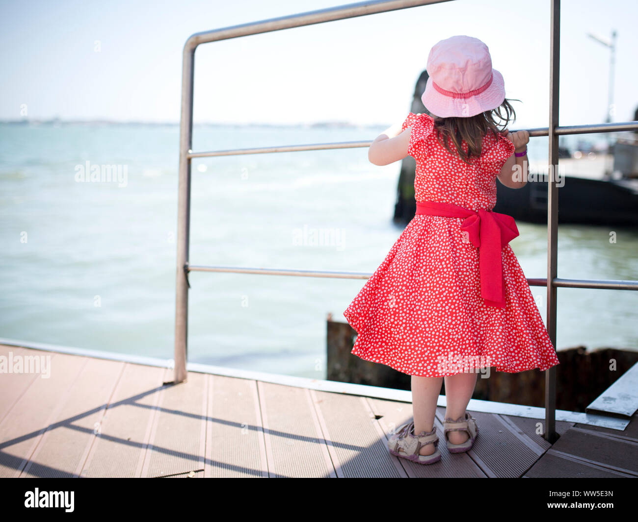 4-6 Jahre altes Kind im roten Kleid an der Anlegestelle wartet Stockfoto