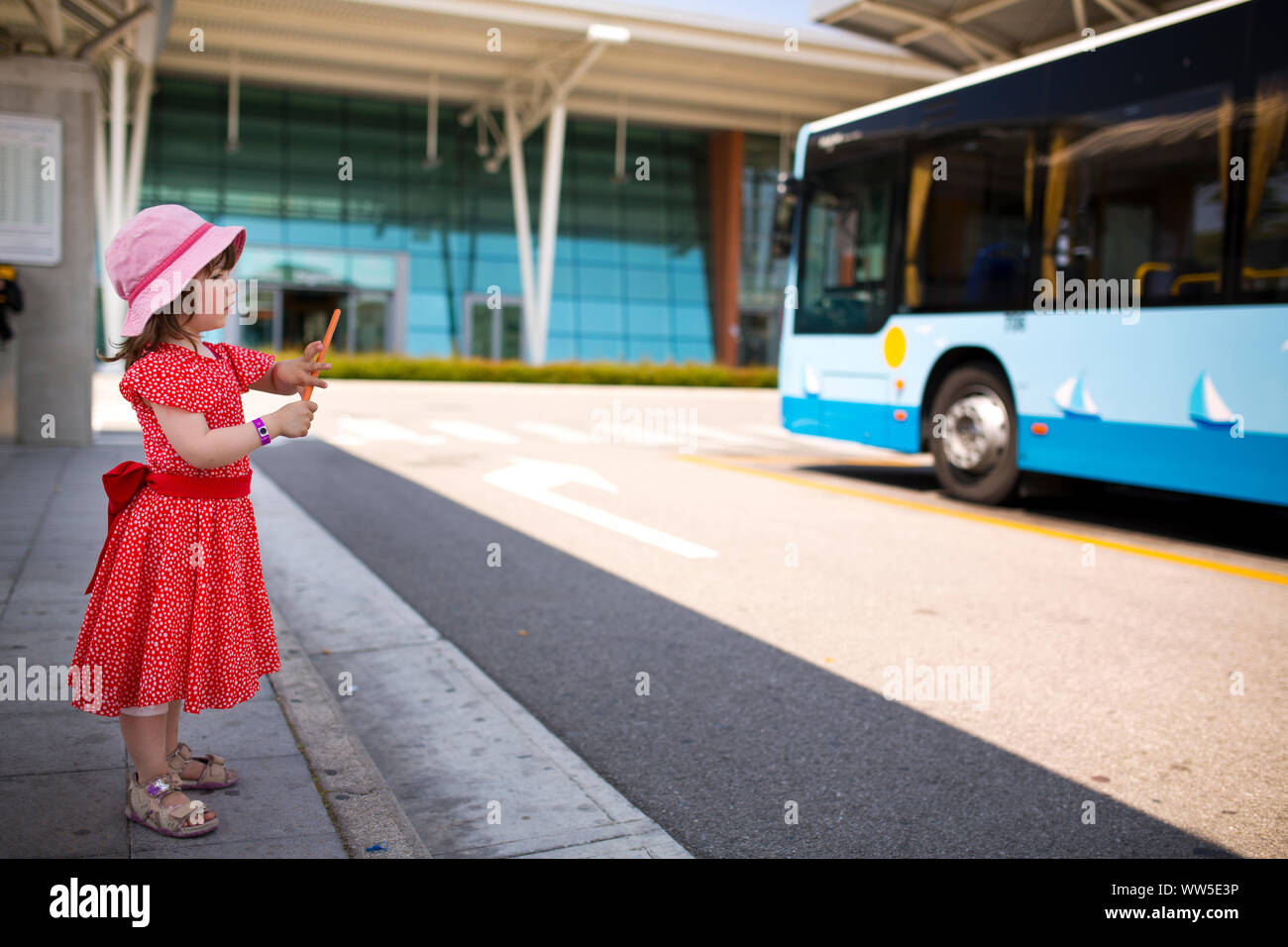 4-6 Jahre altes Mädchen im roten Kleid allein an der Busklemme Stockfoto