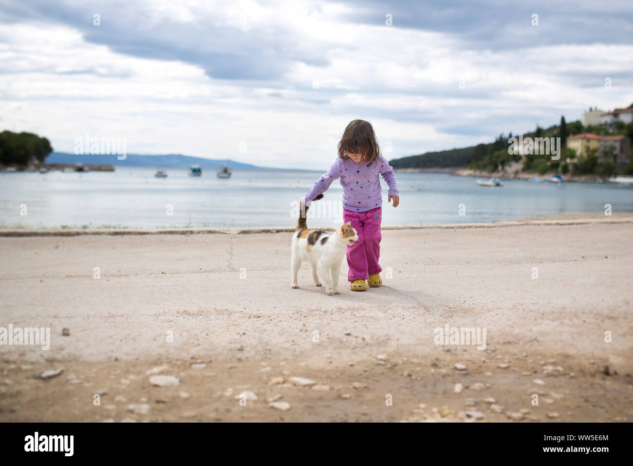 4-6 Jahre altes Kind streichelt die Katze auf dem Kies weg, in einem kleinen Hafen Bucht Stockfoto