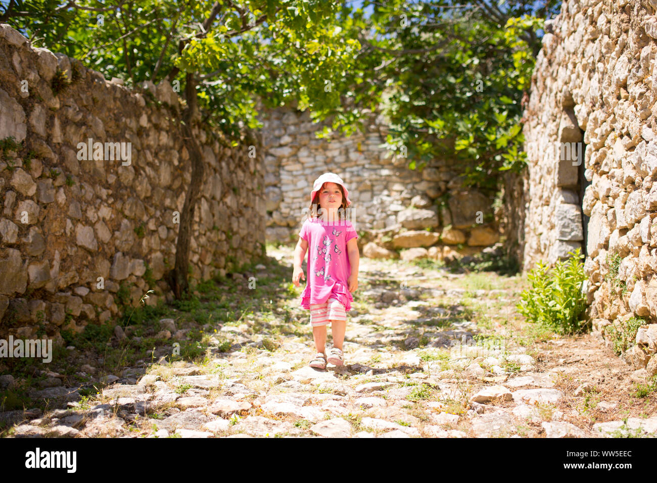 4-6 Jahre alten Mädchen in rosa Outfit entlang einer alten steinigen Weg läuft Stockfoto