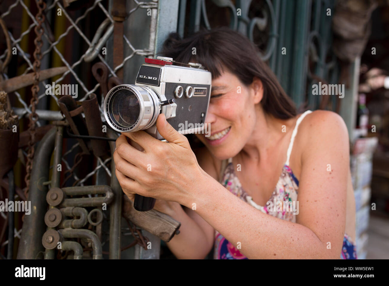 30 bis 40 Jahre alte Frau in Kleid im Metallgitter mit Super8-Kamera in der Hand Stockfoto