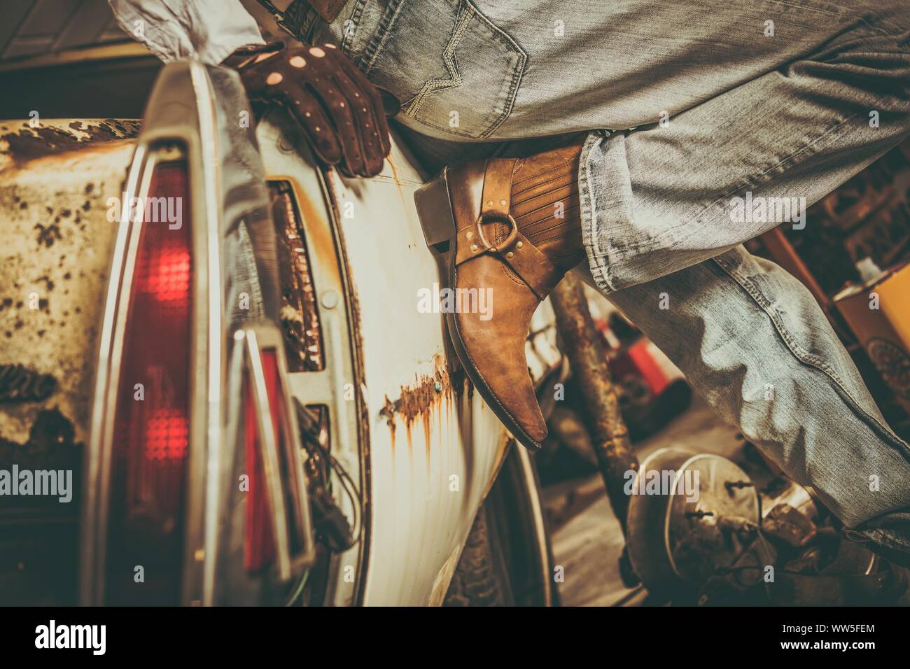 Western Style Jeans und Stiefel. Cowboy und seine rostige beschädigt Auto innen schmutzig Scheune. Untere Partie Nahaufnahme. Stockfoto