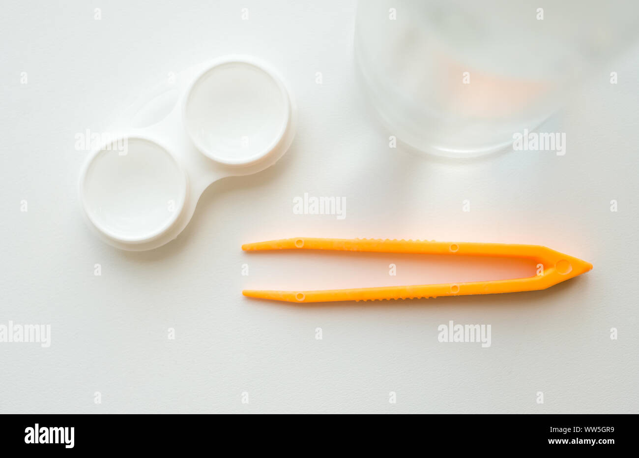 Zubehör für die richtige Verwendung von Kontaktlinsen: Gehäuse, Pinzette und Flasche Lösung auf weißem Hintergrund. Sichere Sehkorrektur. Blick von oben. Stockfoto