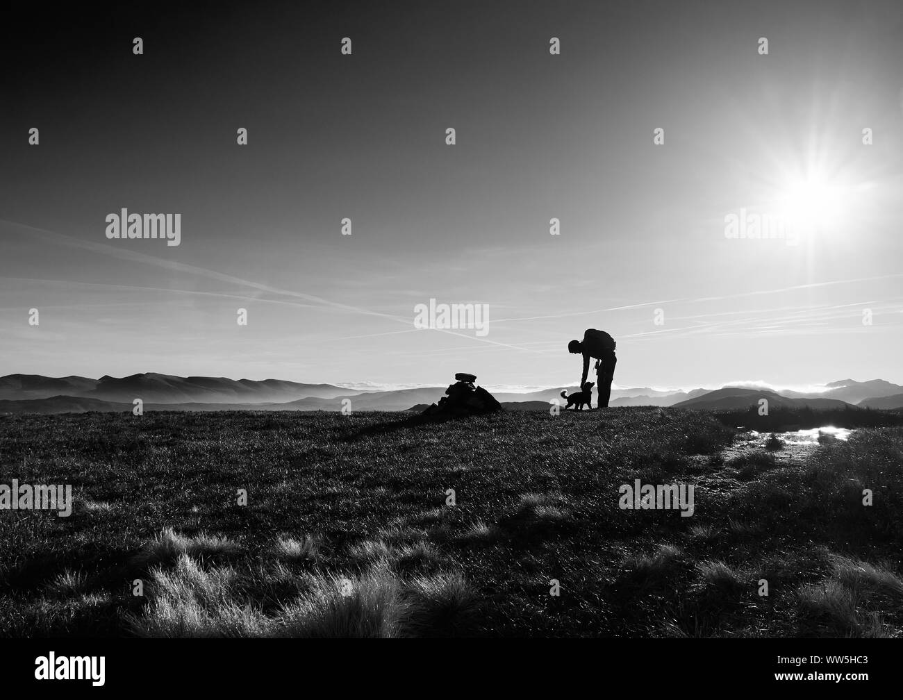 Ein schwarz-weiß Bild von einem Wanderer und ihrem Hund auf einem Gipfel auf einem kalten Wintern morgen im Derwent Fells, Englisch See Distrct, UK. Stockfoto