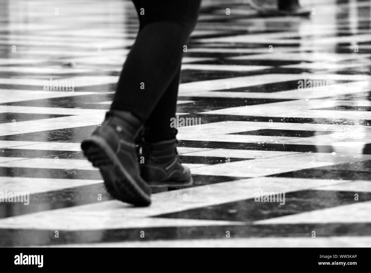 Fotografie von schwarzen und weißen Fliesen- Plattform im Regen mit einem Fußgänger, Stockfoto