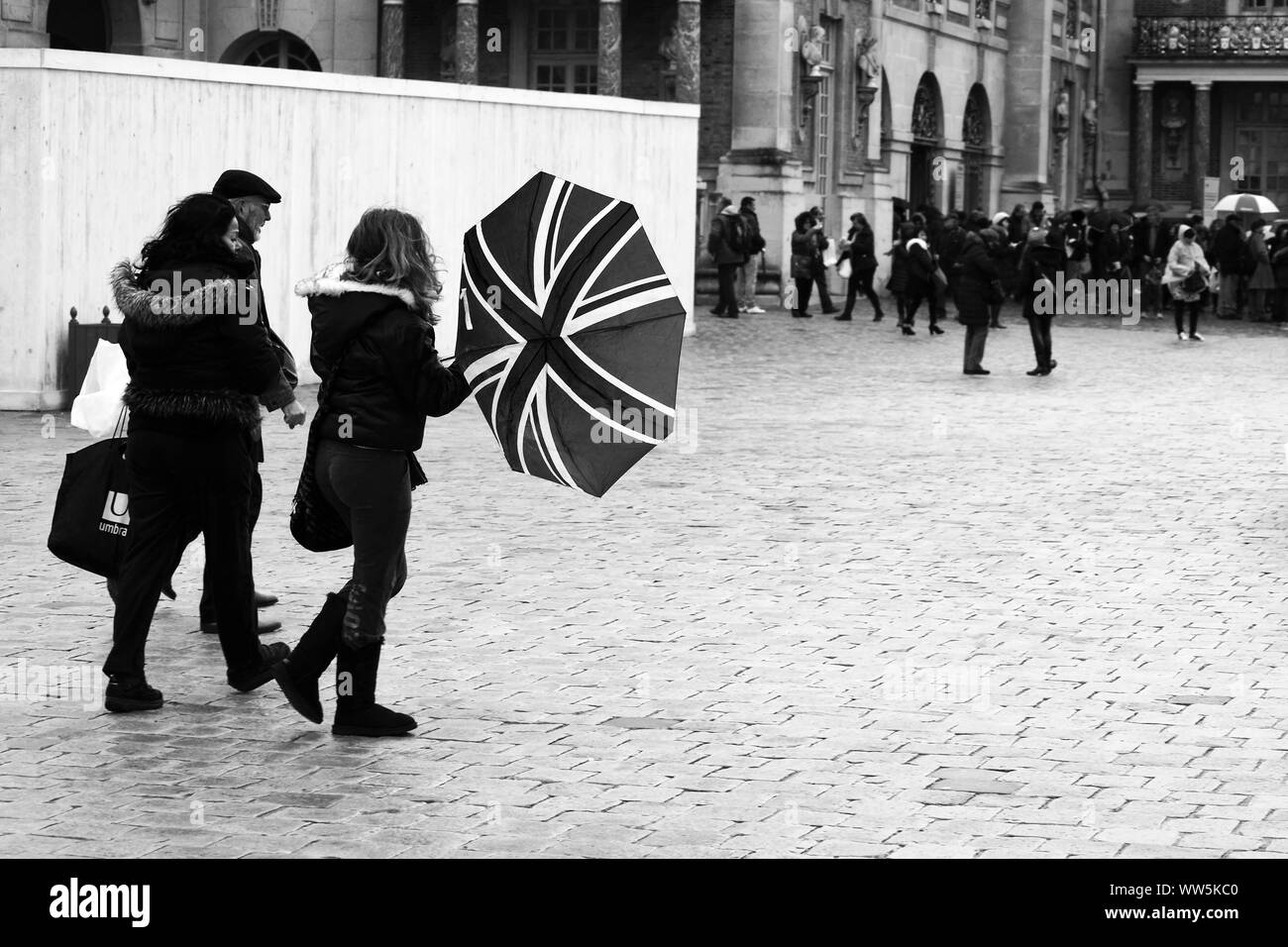 Touristen stehen und gehen im regnerischen Wetter auf dem Platz vor dem Palast von Versailles in Paris, Stockfoto