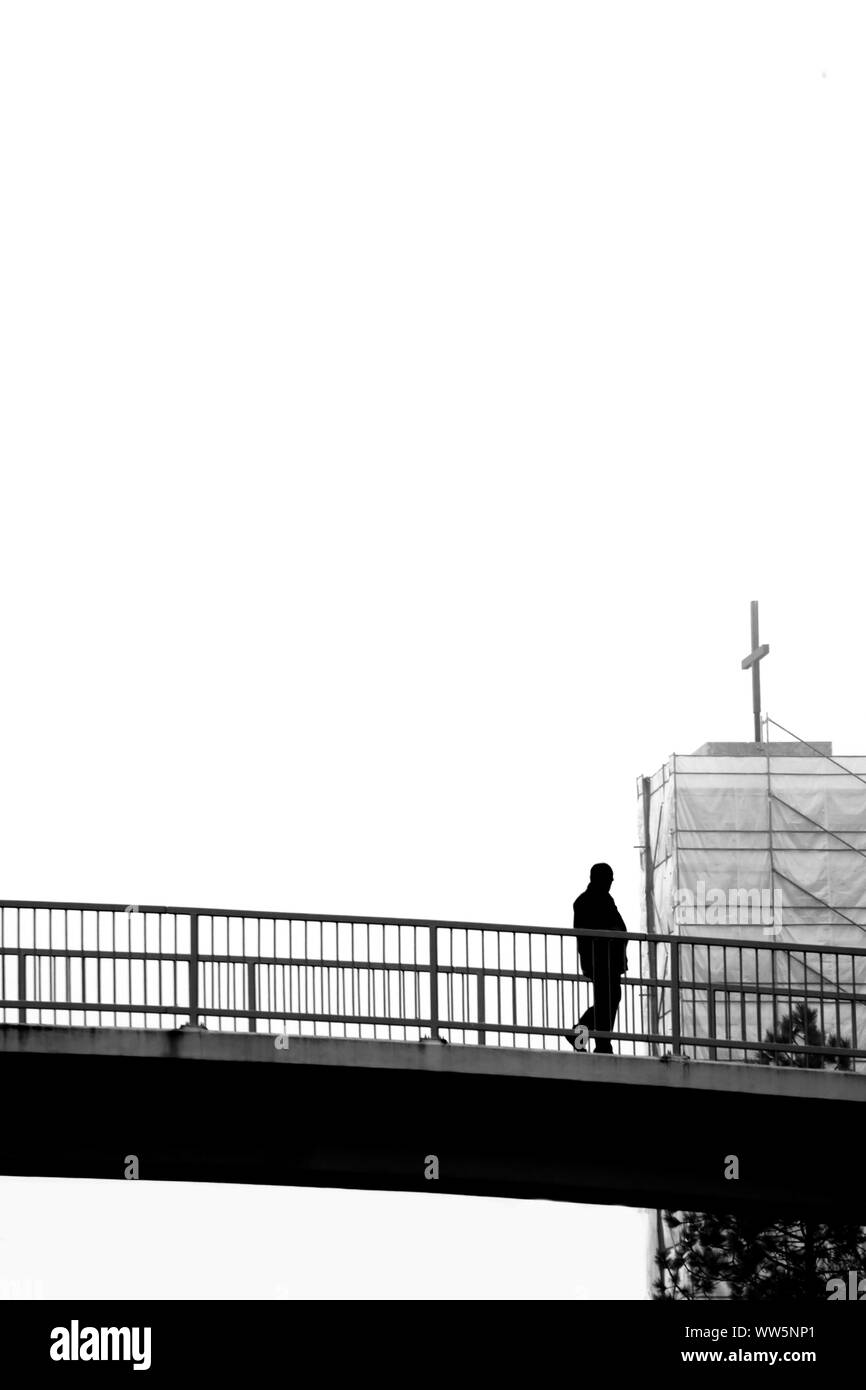 Die freigegebene Schwarzweiß-Fotografie die Silhouette eines Mannes, der über eine Brücke, Stockfoto