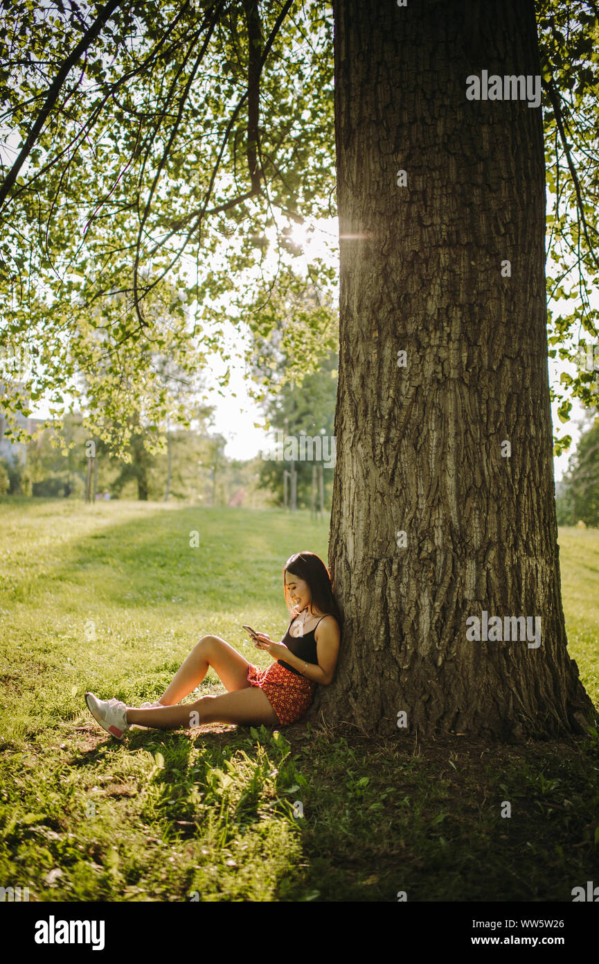 Frau sitzt unter einem Baum auf ihr Mobiltelefon suchen, Serbien Stockfoto