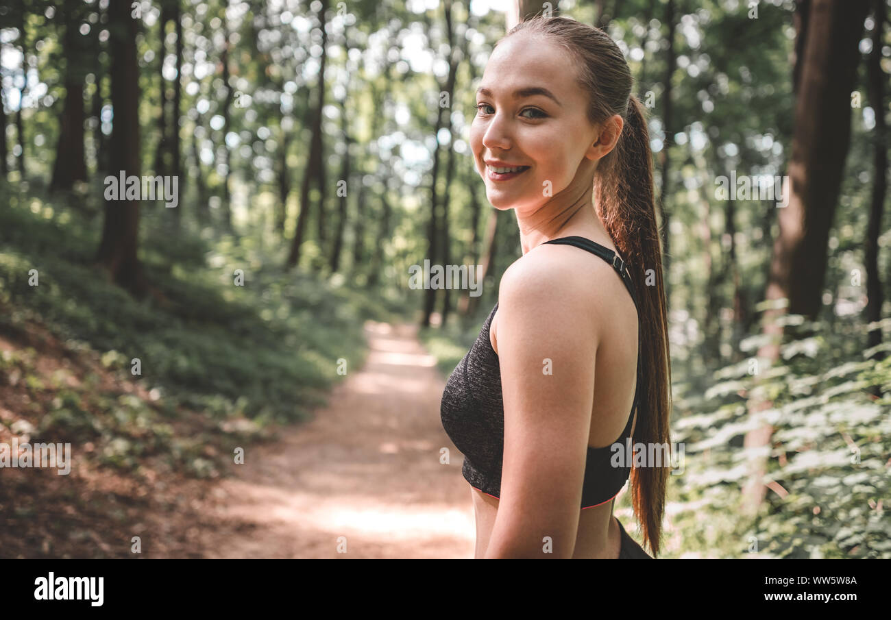 Portrait einer jungen sportliche Frau mit einem Lächeln auf ihrem Gesicht auf in den Wald. Schöne Mädchen suchen und lächelnd in die Kamera vor dem Ausführen Stockfoto