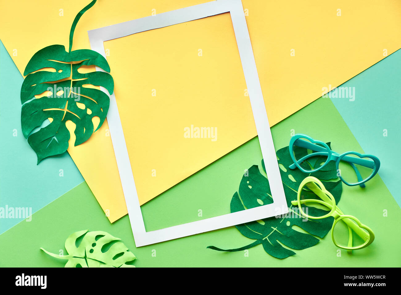 Geometrische flach mit Papier Rahmen, exotische monstera Blätter und herzförmige Sonnenbrille auf geometrische Mint, grün und gelb Papier Hintergrund Stockfoto