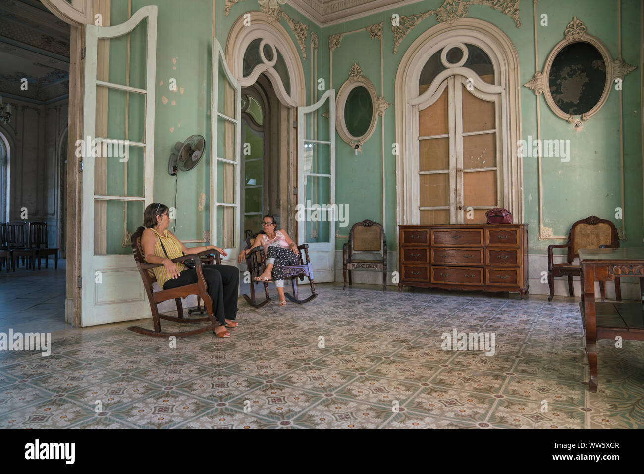 Palacio Ferrer wurde in 1917/18 von Spanischen squire JosÃ© Ferrer, heute ist das Gebäude für die Öffentlichkeit, das Bild zeigt ein Zimmer des Palacio mit Inneneinrichtung und zwei 'Museum Assistenten' im Schaukelstuhl, Cienfuegos, Kuba gebaut Stockfoto