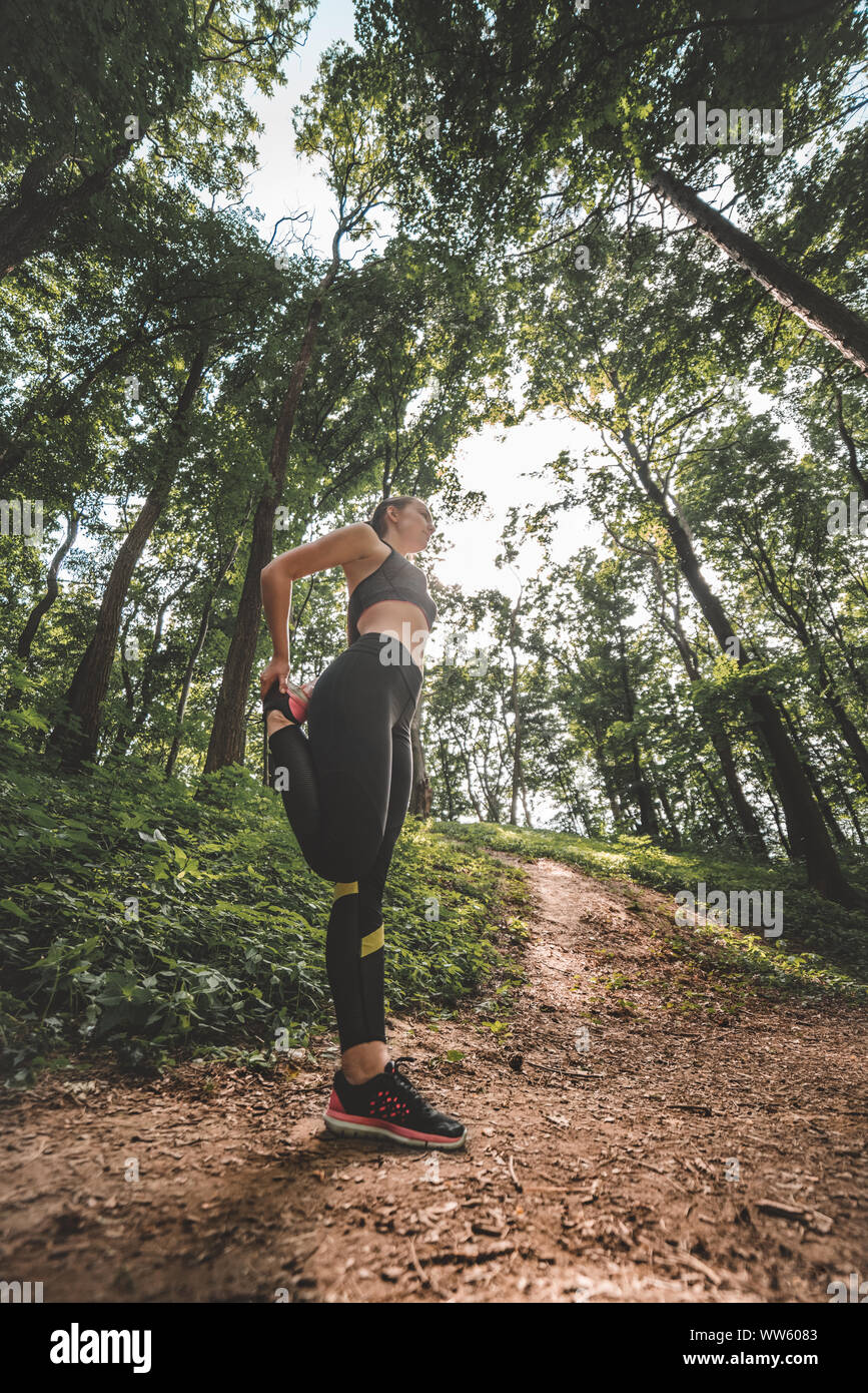 Low Angle Image der jungen Sportlerin und Warm-up vor dem Training im Wald. Seitenansicht des slim fit female Vorbereitung auf den Waldweg zu starten Stockfoto