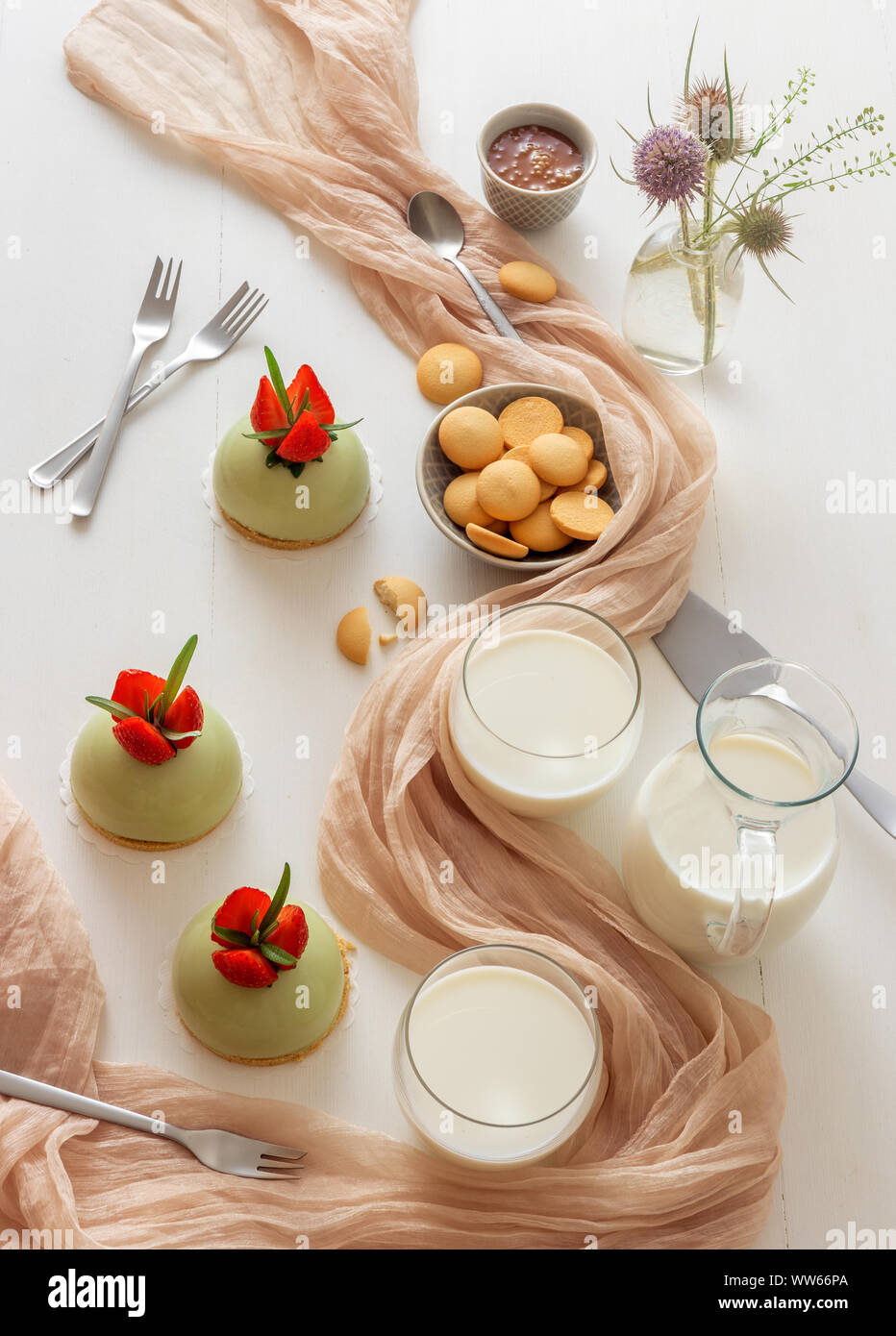 Weiße Holztisch mit 3-Backen Erdbeere mini Kugel matcha Käsekuchen mit Schale mit Salz Karamell und buiscuits, Glas Plätze und ein Glas Milch. Stockfoto