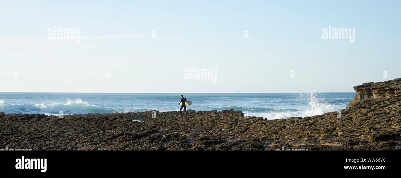 Mann, Surfbrett über Fels in der Brandung vom Meer Stockfoto