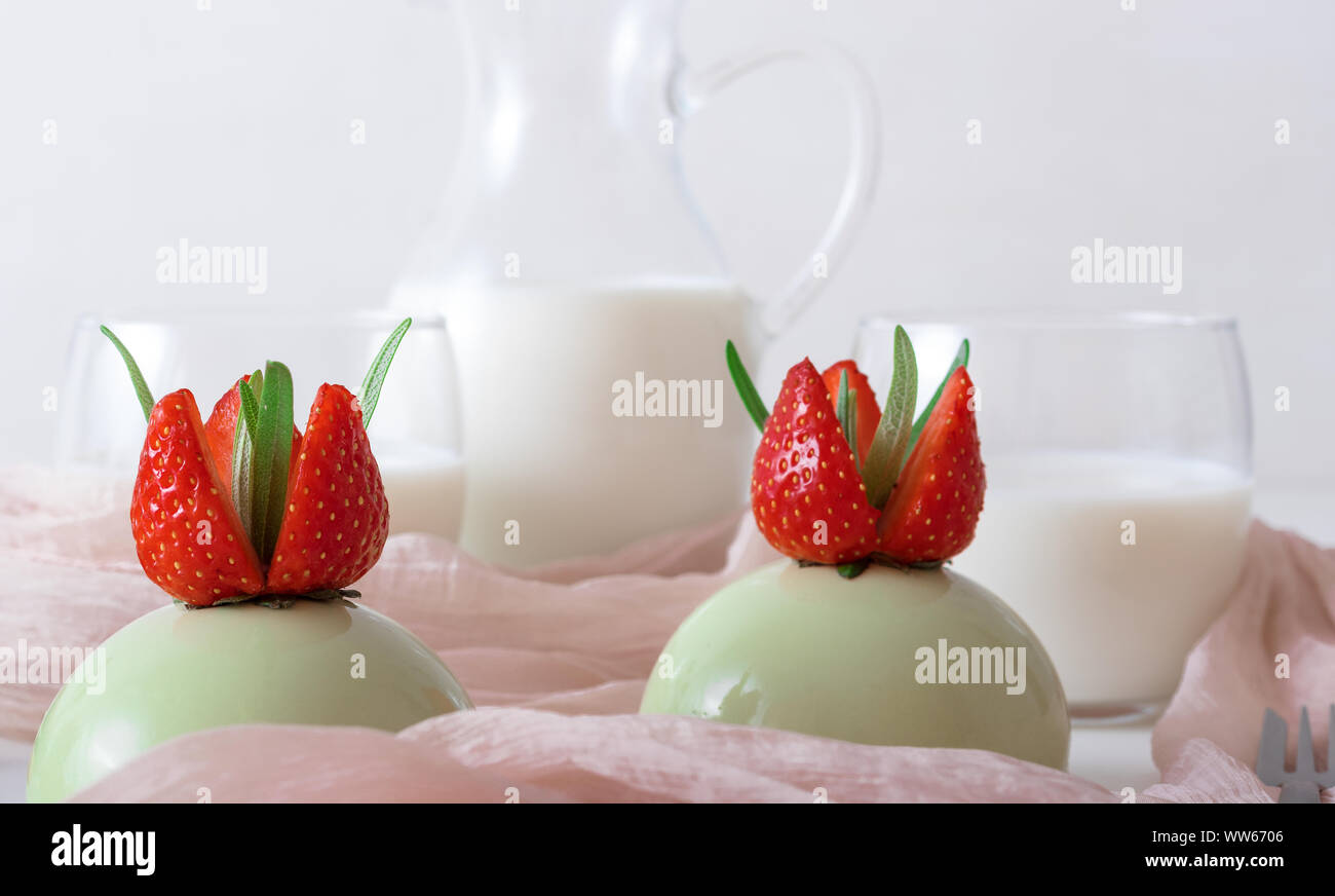 Matcha Käsekuchen. Weiße Holztisch mit 2-Backen Erdbeere mini Kugel Käsekuchen mit Schale mit Salz Karamell und buiscuits, Glas Plätze und gl Stockfoto