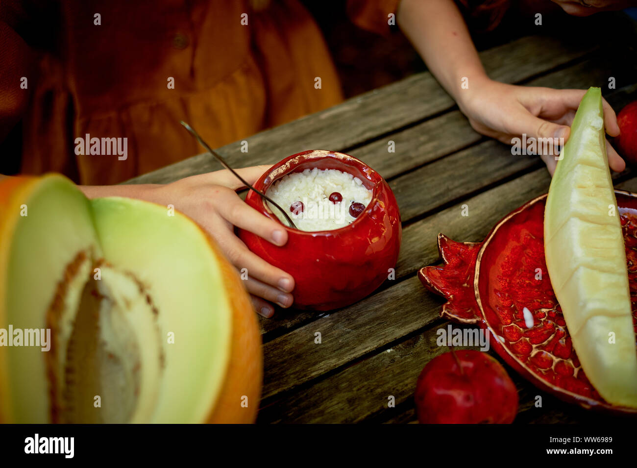 Rote Keramik, handgemacht.geformt wie eine Granate. Kinderhände um den Topf mit Haferbrei. Gesundes Frühstück Stockfoto