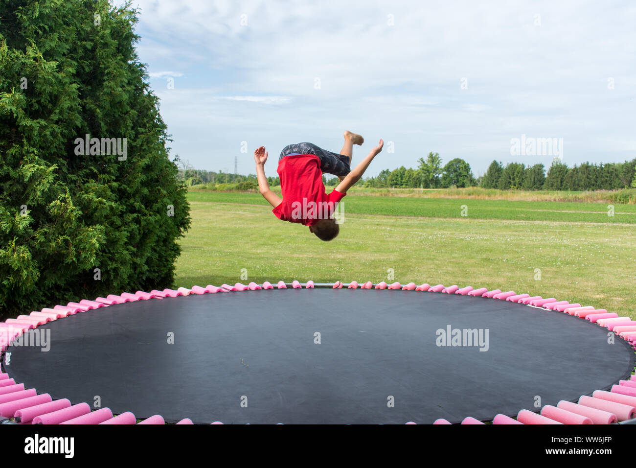 Der Junge im roten Hemd im Freien dreht sich in einem Salto, der eine Gymnastikbewegung auf einem Trampolin macht. Konzept. Stockfoto