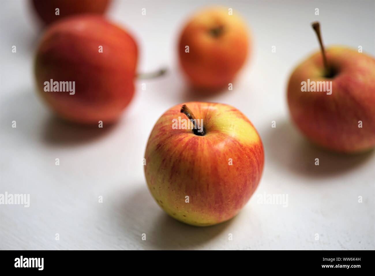 Fünf Äpfel, rot mit gelben Flecken, liegen auf einem weißen Tisch Stockfoto