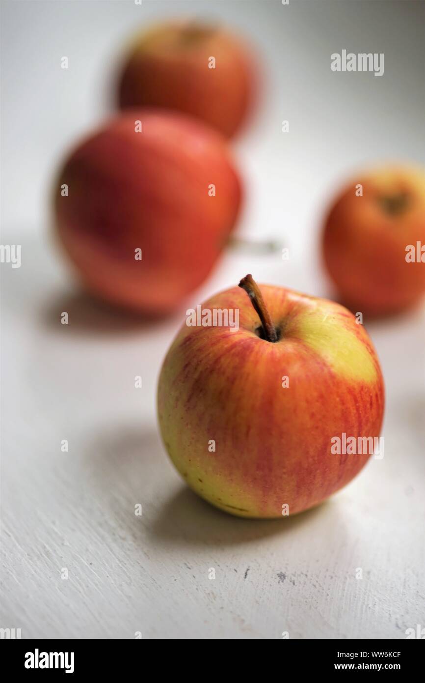 Fünf reife Äpfel, rot mit gelben Flecken, liegen auf einem weißen Tisch Stockfoto
