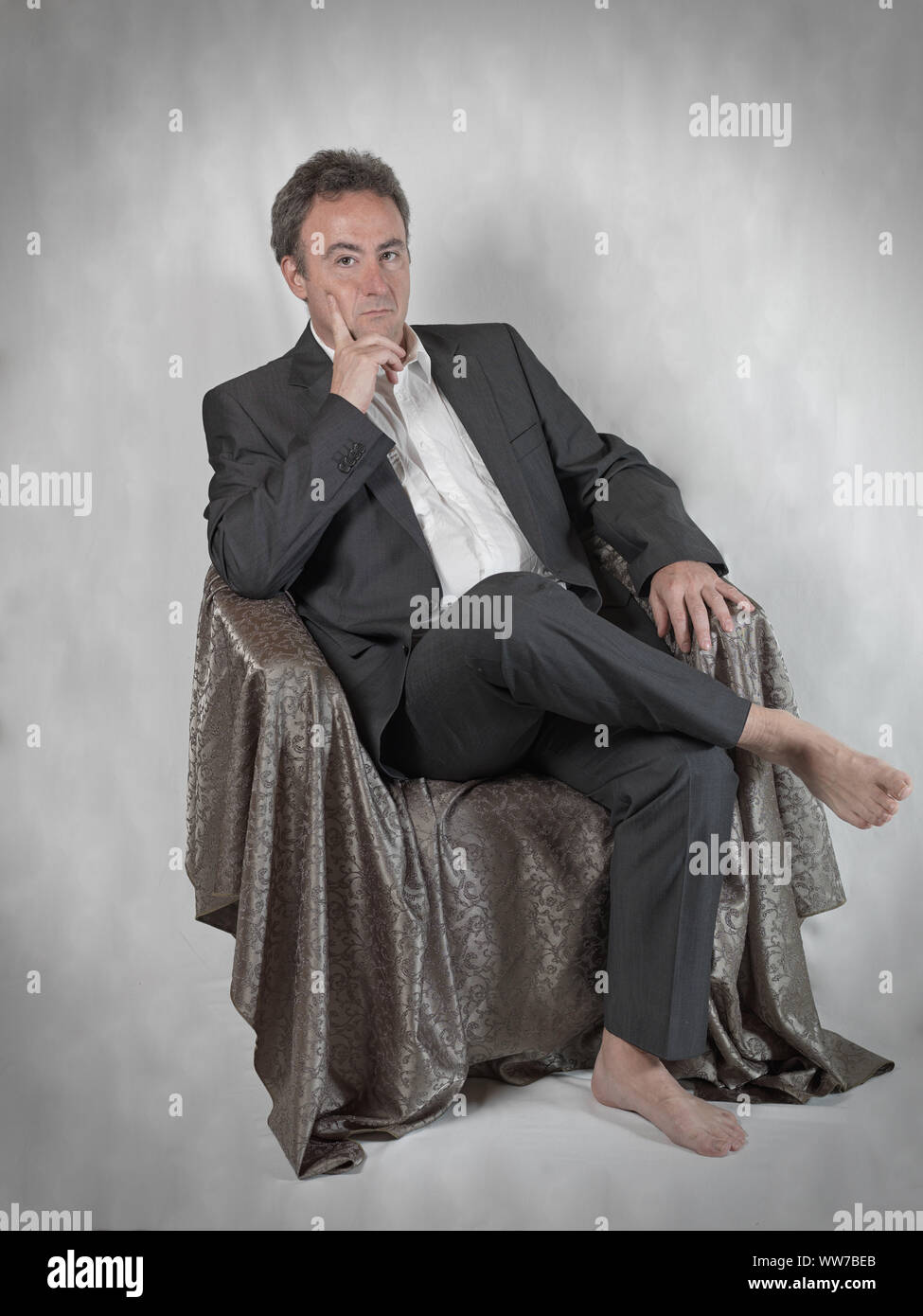 Mann im Anzug aber barfuss, sitzen im Stuhl und sieht nachdenklich aus. Stockfoto