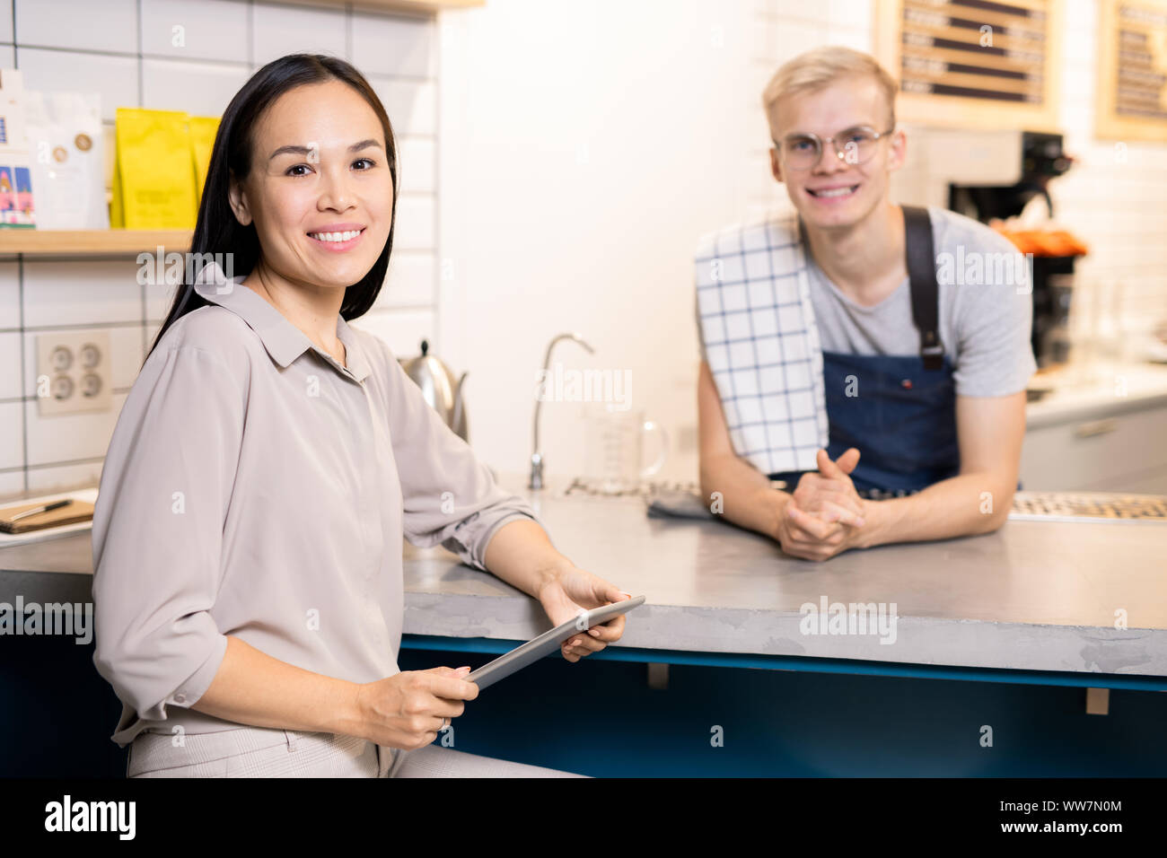 Junge lächelnde Kellnerin und ihr Kollege in Arbeitskleidung warten auf neue Gäste Stockfoto