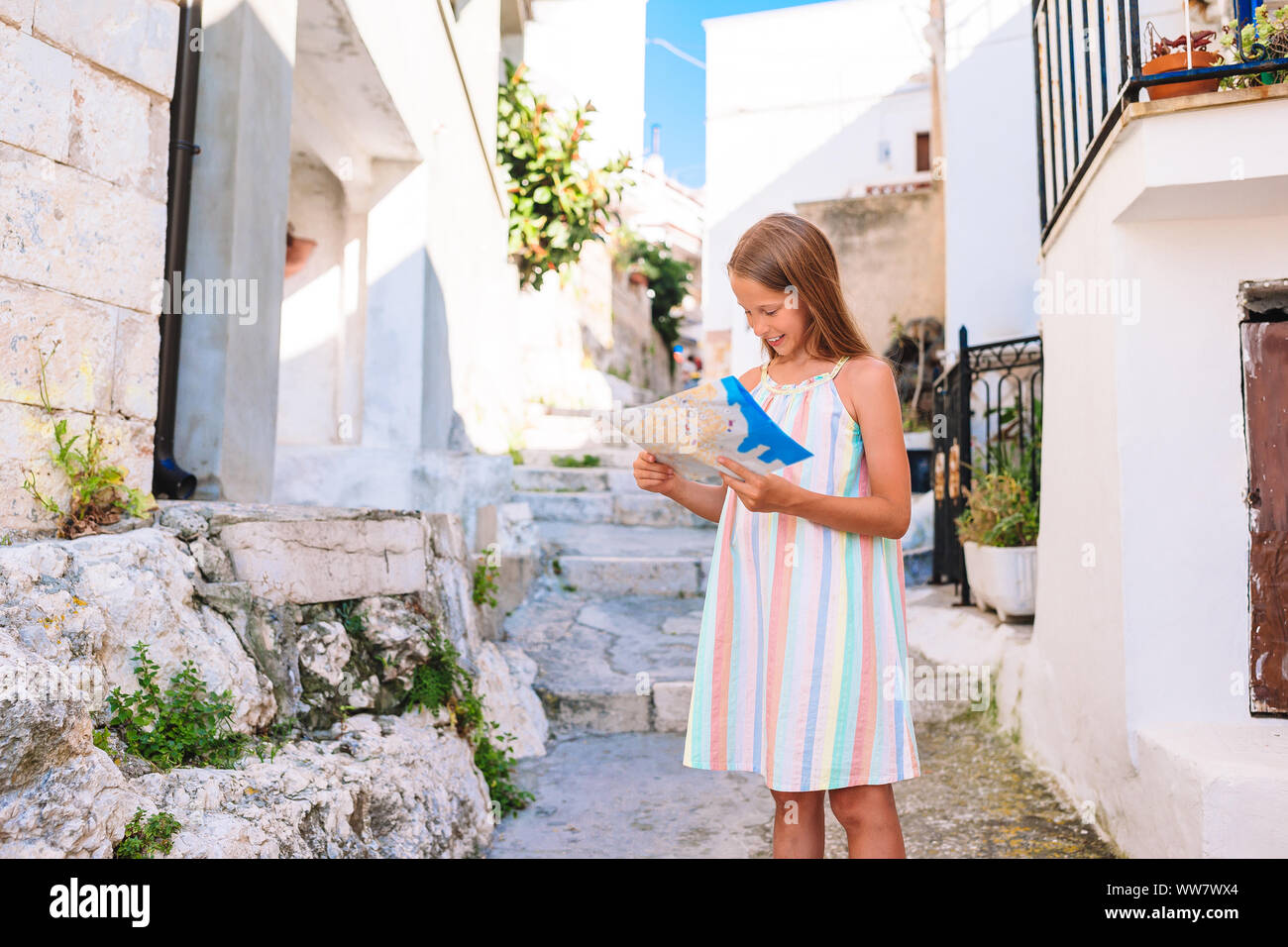 Adorable kleine Mädchen an der alten Straße von typischen griechischen traditionellen Dorf mit weißen Wänden und blauen Türen Stockfoto