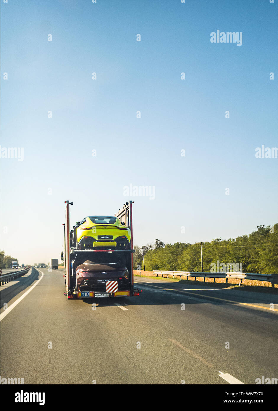 2018: Rack-Truck bewegt sich entlang landschaftlich schöner Autobahn beladen mit Aston Martin Sportwagen Stockfoto