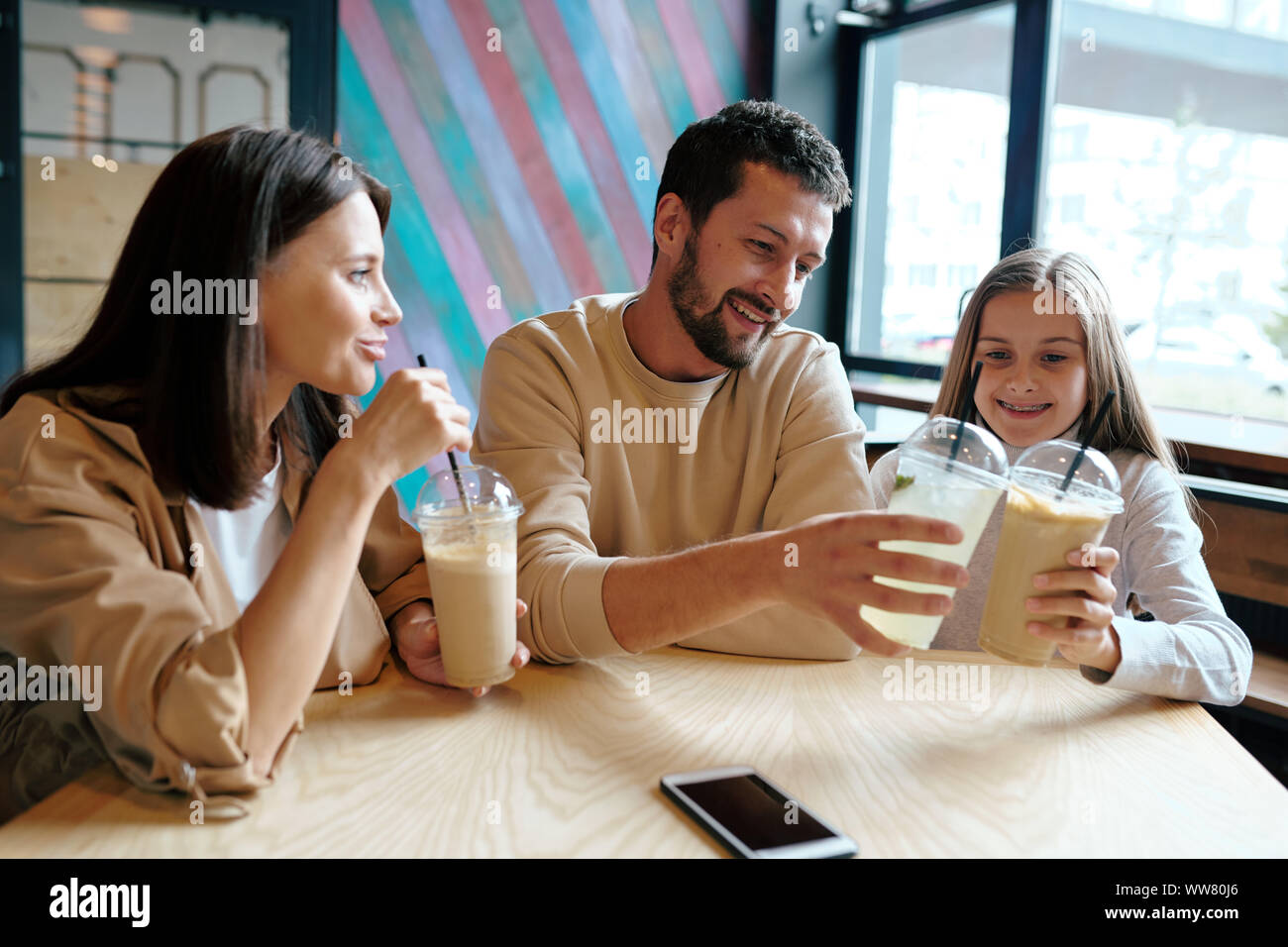 Junger Mann und seine Tochter klirren mit Kunststoff Gläser Milch cocktail Stockfoto