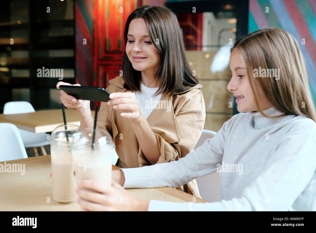 Hübsche junge brünette Frau mit Smartphone, Foto von zwei Milch cocktails Stockfoto