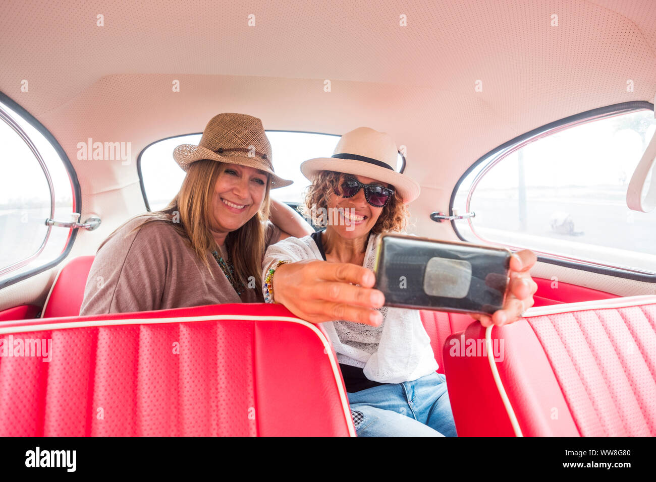 Paar der kaukasischen mittleren Alter Frau in Outdoor Freizeitaktivitäten Aktivität in der Nähe von und sitzen auf einem roten Oldtimer bereit zu reisen, Stockfoto