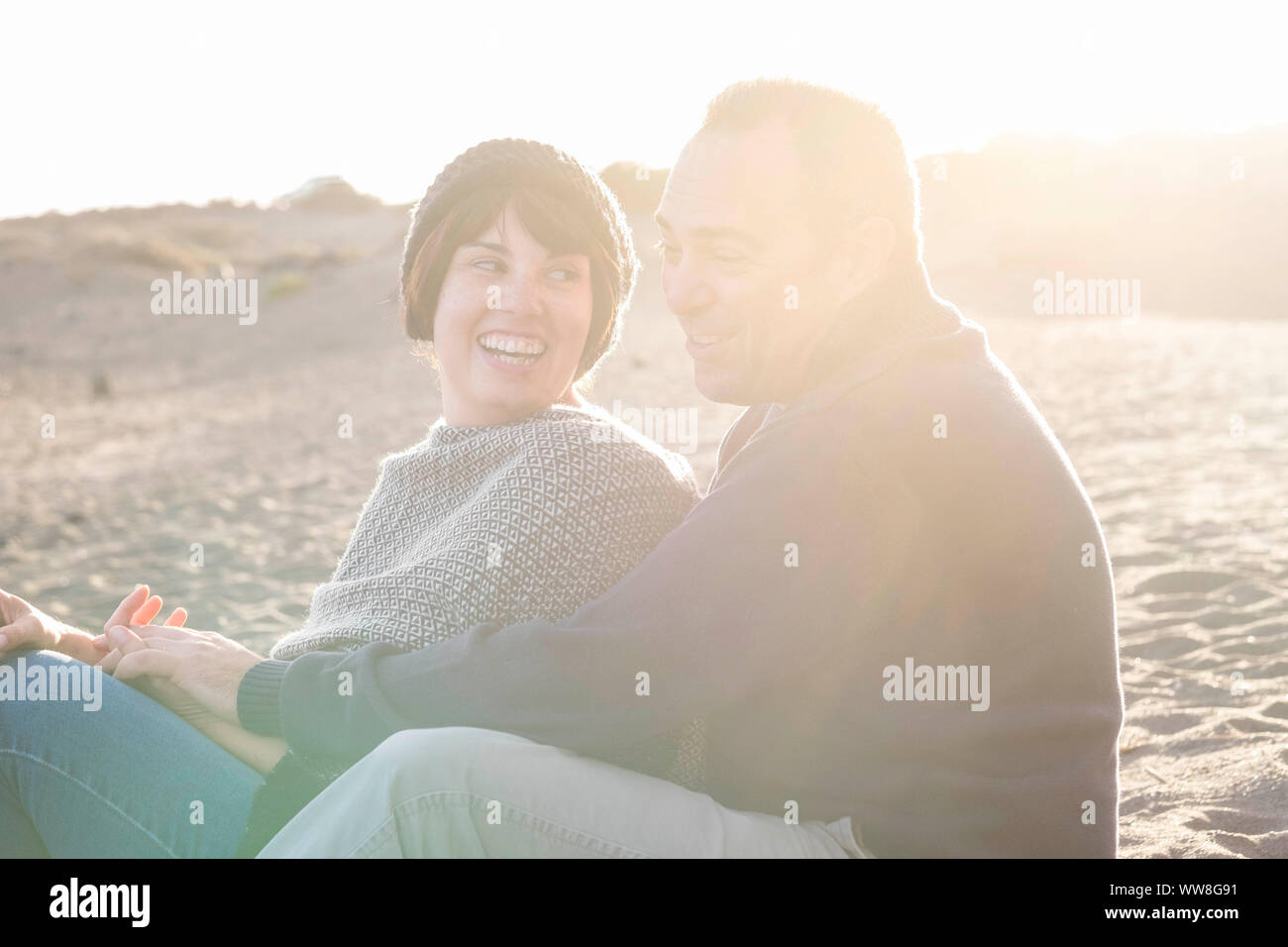 Schöne schöne Mitte Alter 40 Jahre alte Paar Mann und Frau kaukasischen umarmte und zusammen am Strand im sand sitzen und genießen einen goldenen Sonnenuntergang für schöne Freizeitaktivitäten Aktivität draußen in der Natur übernachten Stockfoto