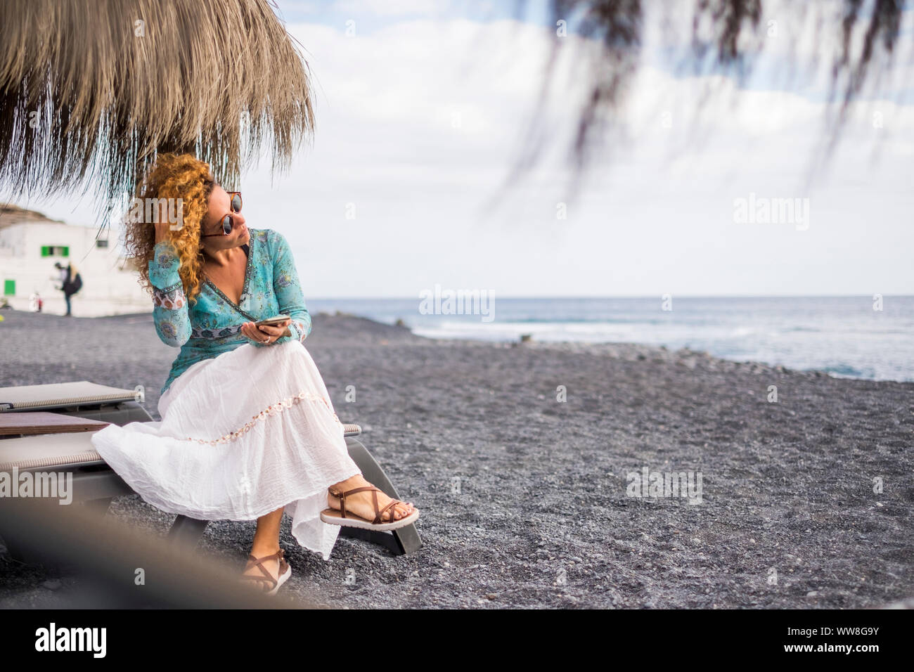 Schöne junge Frau mit Handy am Strand im Urlaub Freizeit am Strand, das Meer und die Wellen im Hintergrund, während Sie ihre Lockige braune Haare, Sonnenbrille auf Schönheit Gesicht Stockfoto