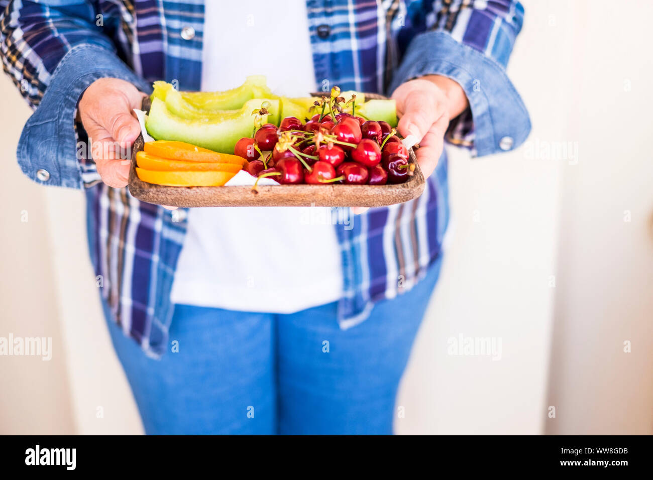 Alte kaukasische Frau senior kaukasischen in lässigen Jeans Kleidung bieten einige frische Früchte der Saison für Sie, Melone, Orange und Kirsche für eine gemischte Farben essen, um gesund zu bleiben und einen schönen Lebensstil haben Stockfoto