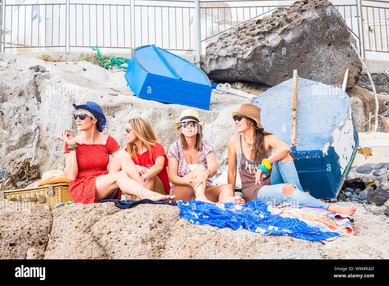 Gruppe von Frauen Freunde sitzen auf den Felsen in der Nähe des Meeres und genießen Sie Urlaub und Freizeit Outdoor Aktivität Entspannung in Freundschaft. glücklich Lifestyle Menschen, vier Frauen, die zusammen unter der Sommersonne Aufenthalt Stockfoto